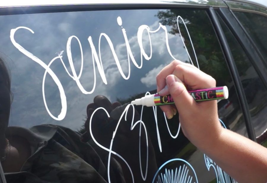 A+senior+decorates+with+white+markers+on+their+car+window+before+the+parade.